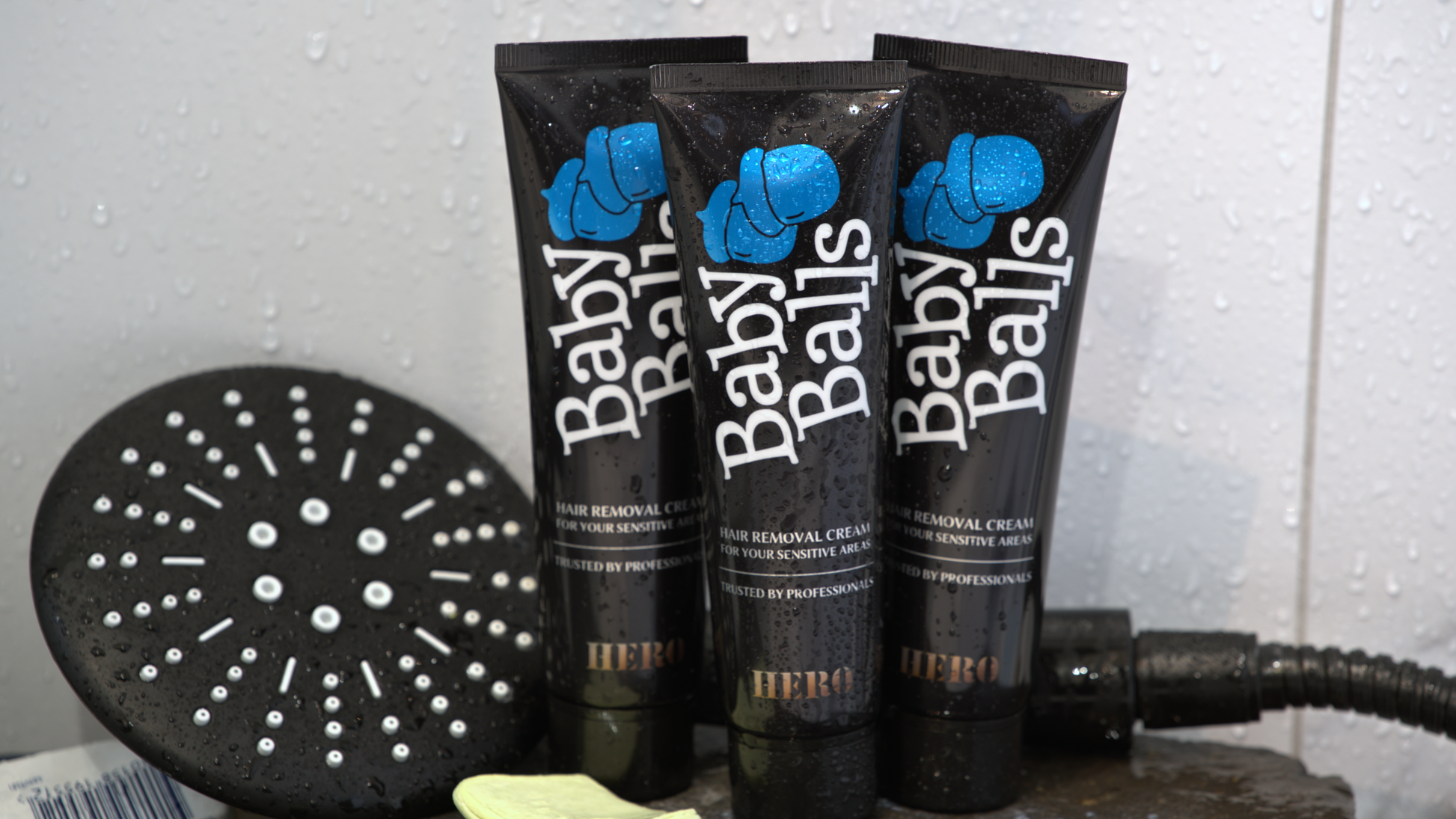 Three tubes of mens 'Baby Balls' hair removal cream with a shower head in the background.